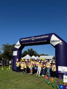Participants wearing matching yellow shirts gather at the finish line under a large purple inflatable arch reading “Alzheimer’s Association” and “FINISH” during a Walk to End Alzheimer’s event.