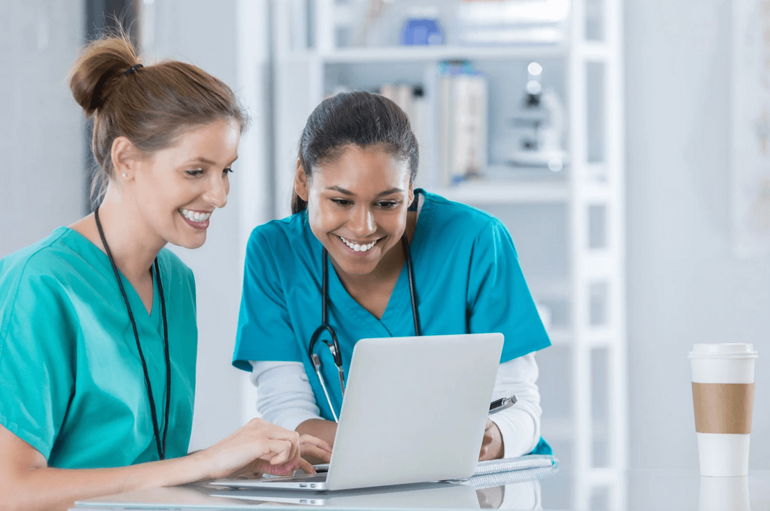 Two nurses reviewing healthcare compliance standards and regulations on laptop