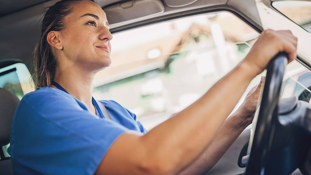 Home health driving safety: clinician in scrubs driving to a patient visit with her eyes on the road